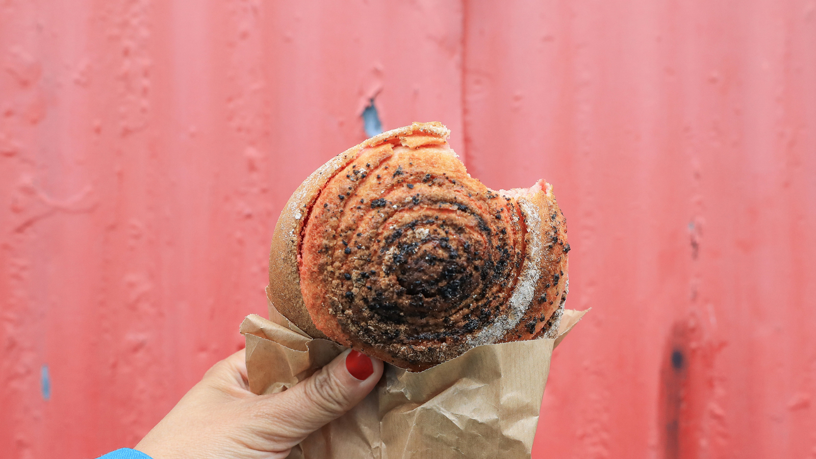 A person holding a cinnamon roll with a red background