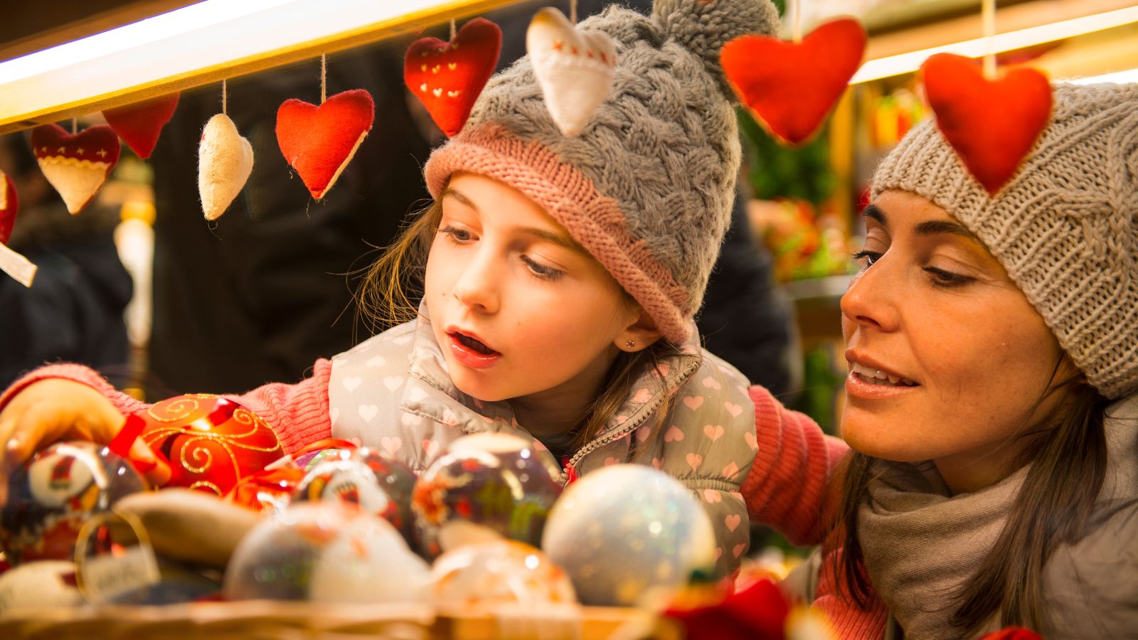 A mother holding her daughter as she looks at decorations at a Christmas market.