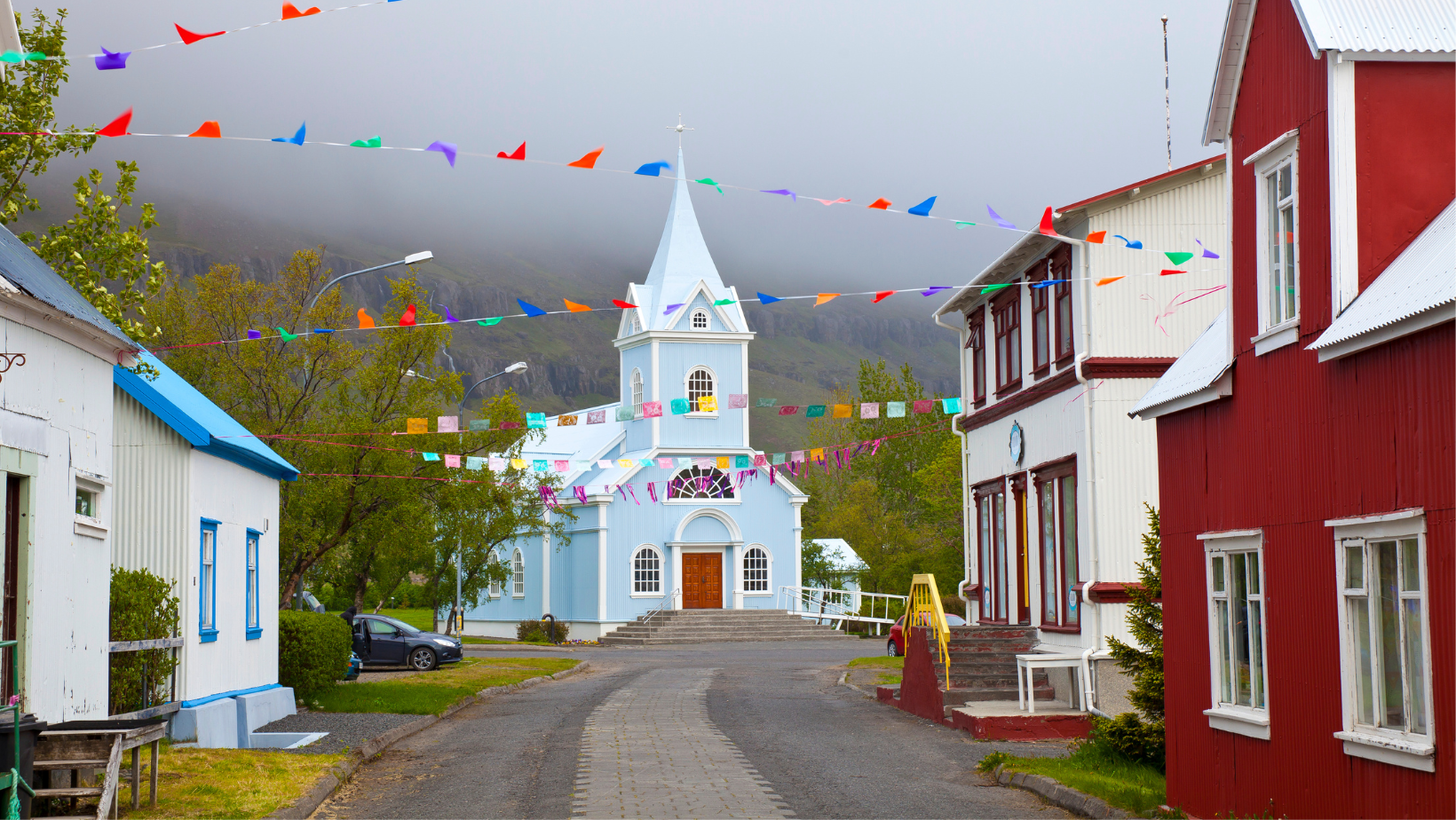 The famous blue church in Seyðisfjörður with a rainbow road painted towards it 