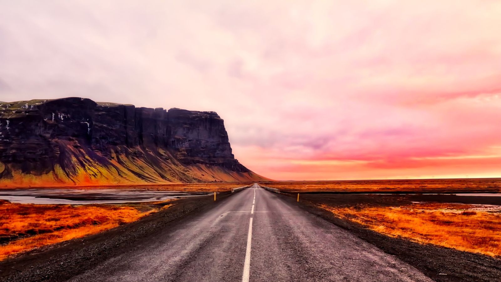 A highway in Iceland with rocky mountains and pink skies in the background.